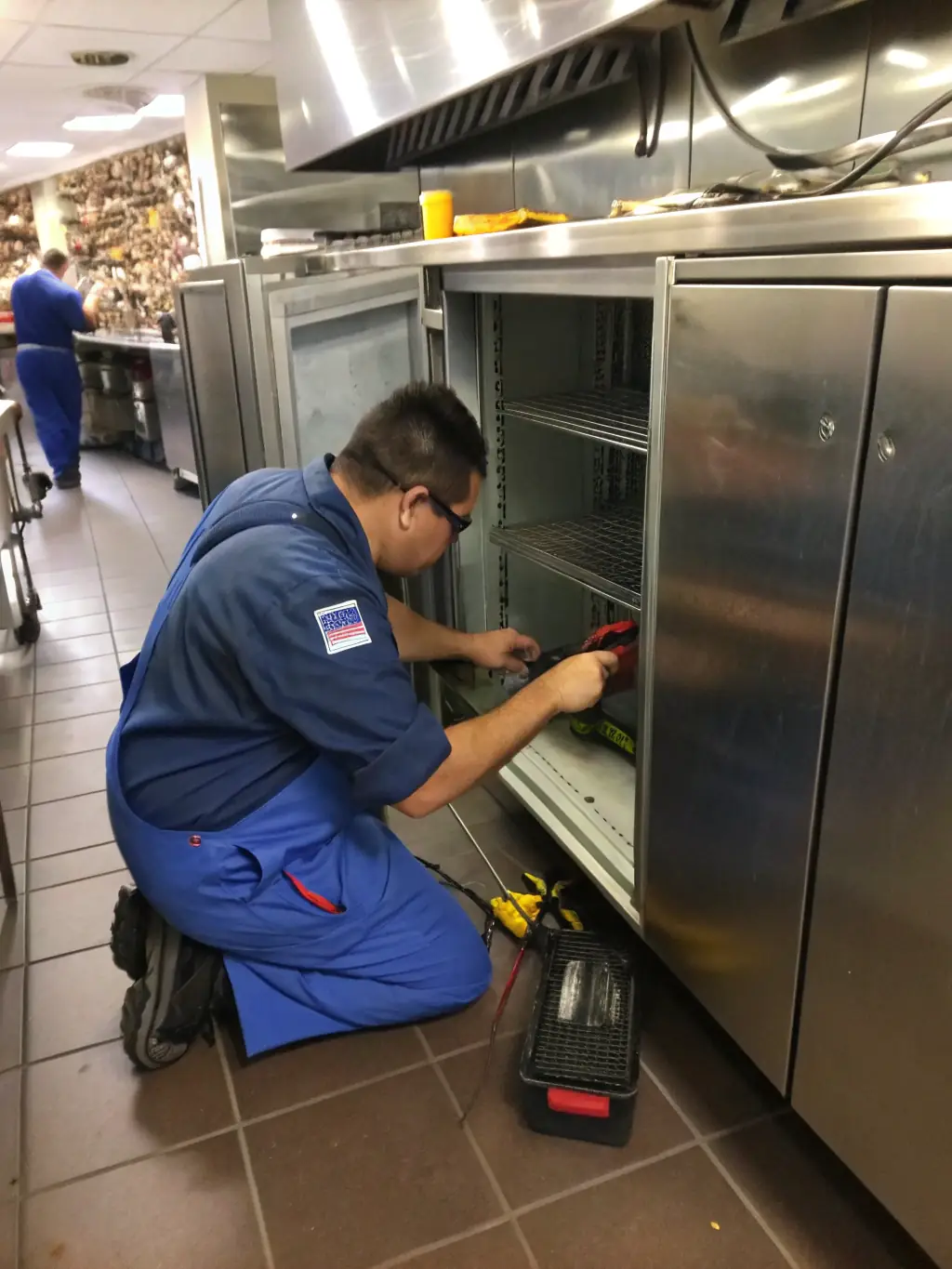 A technician in a grocery store repairing a commercial refrigeration unit, highlighting the importance of maintenance and repair.